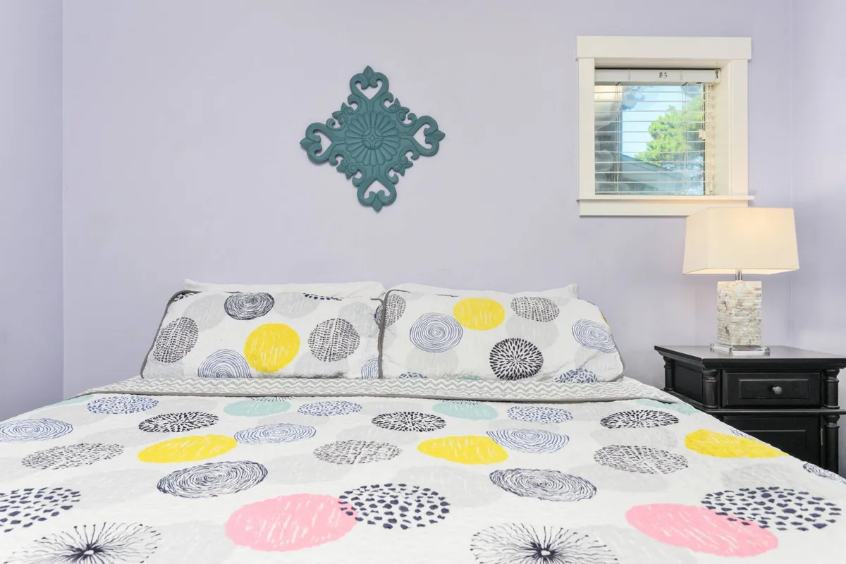 A cozy bed with a patterned quilt sits near a window, decorated with cheerful wall art and a table lamp. The playful, inviting mood is perfect for children’s reading or quiet moments.