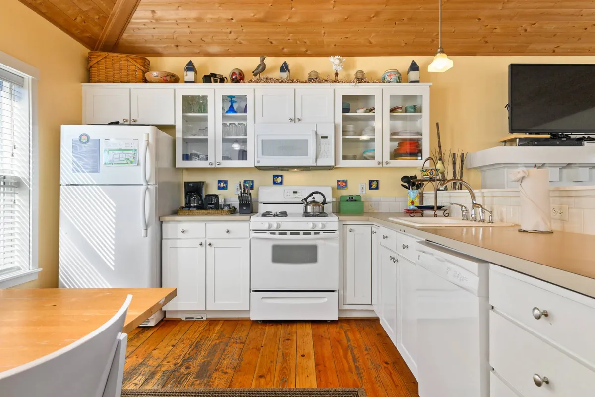 A close-up view of the kitchen, showcasing white cabinetry, wooden countertops, a central kitchen island, and decorative open shelving. The mood is cozy and welcoming, suggesting a space that’s perfect for shared cooking and casual gatherings.