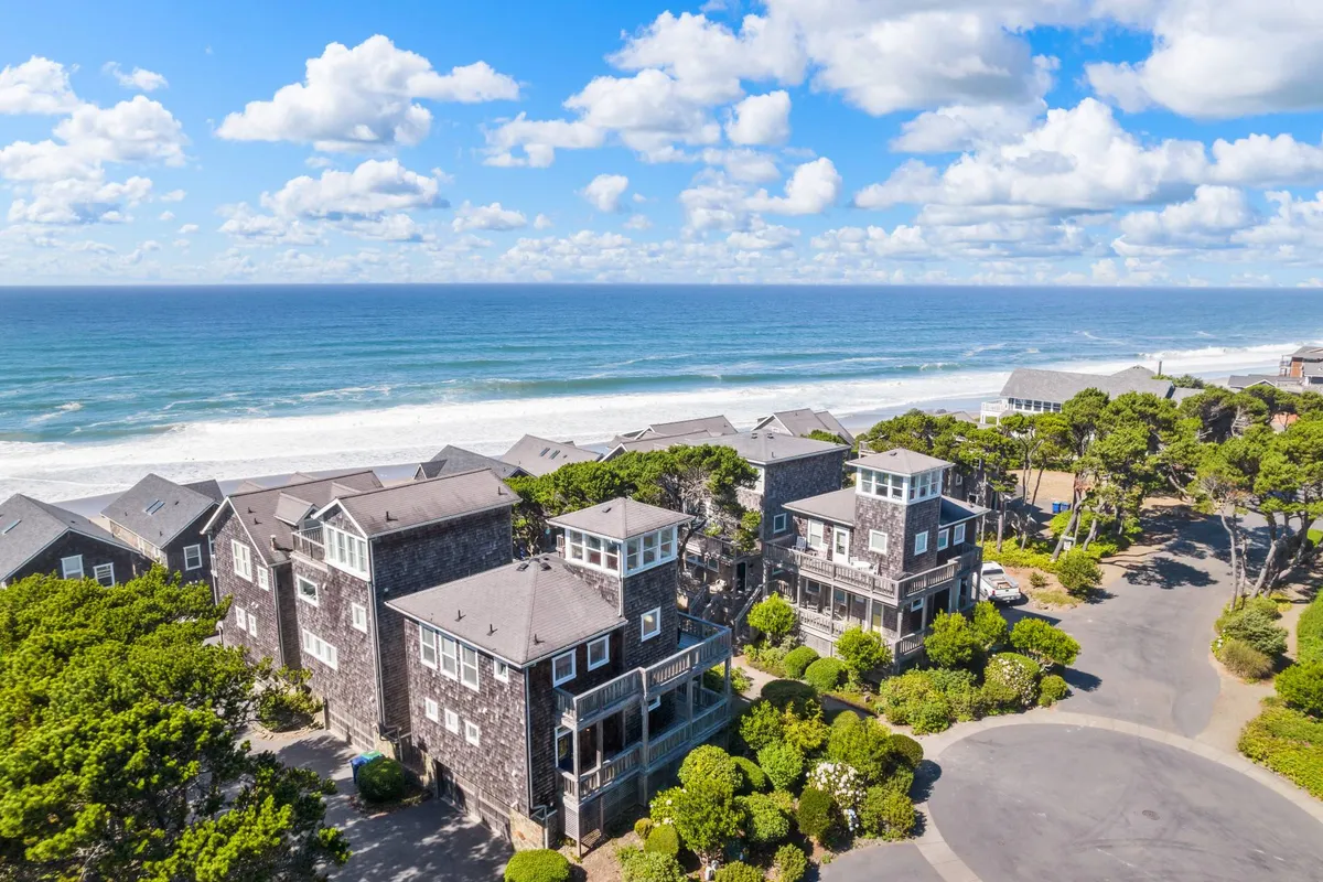 A serene exterior view featuring the ocean, a tree line, and charming coastal architecture. The buildings' details are visible, suggesting a peaceful neighborhood with easy access to the beach, ideal for evening strolls and family gatherings.