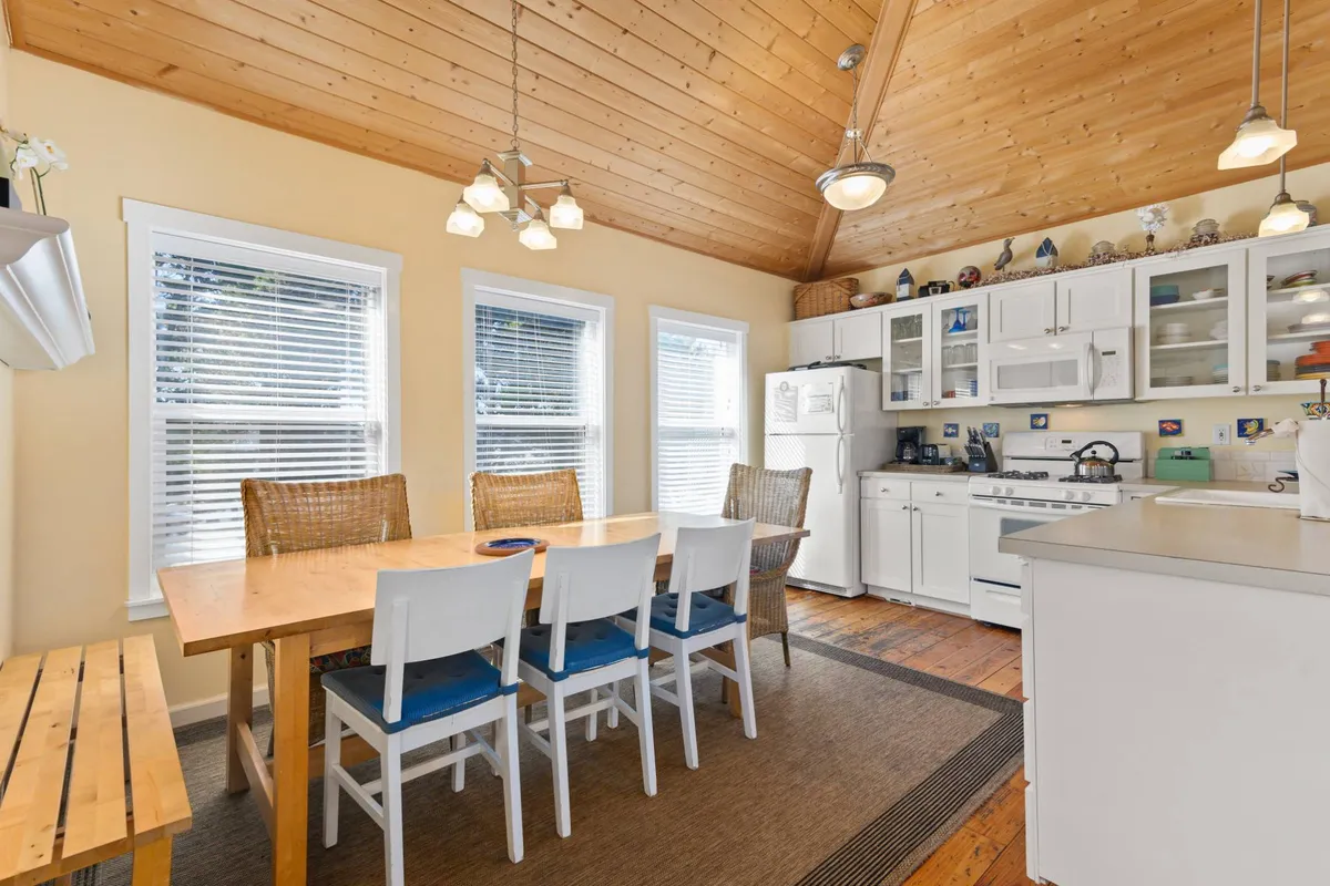 This image showcases an airy dining space with a large table, kitchen appliances, expansive windows, and a wooden ceiling. The ambiance is warm and communal, suggesting gatherings and activities such as family game nights, which are highlighted in the text. The windows subtly reference the expansive views available throughout the home.