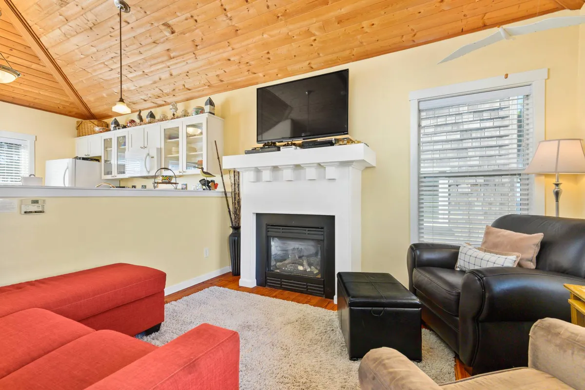 A warm living room scene with a red sectional sofa, a glowing gas fireplace with a TV mounted above, a black leather chair, and a soft rug. The space looks perfect for movie nights, gaming, or cozying up with loved ones.