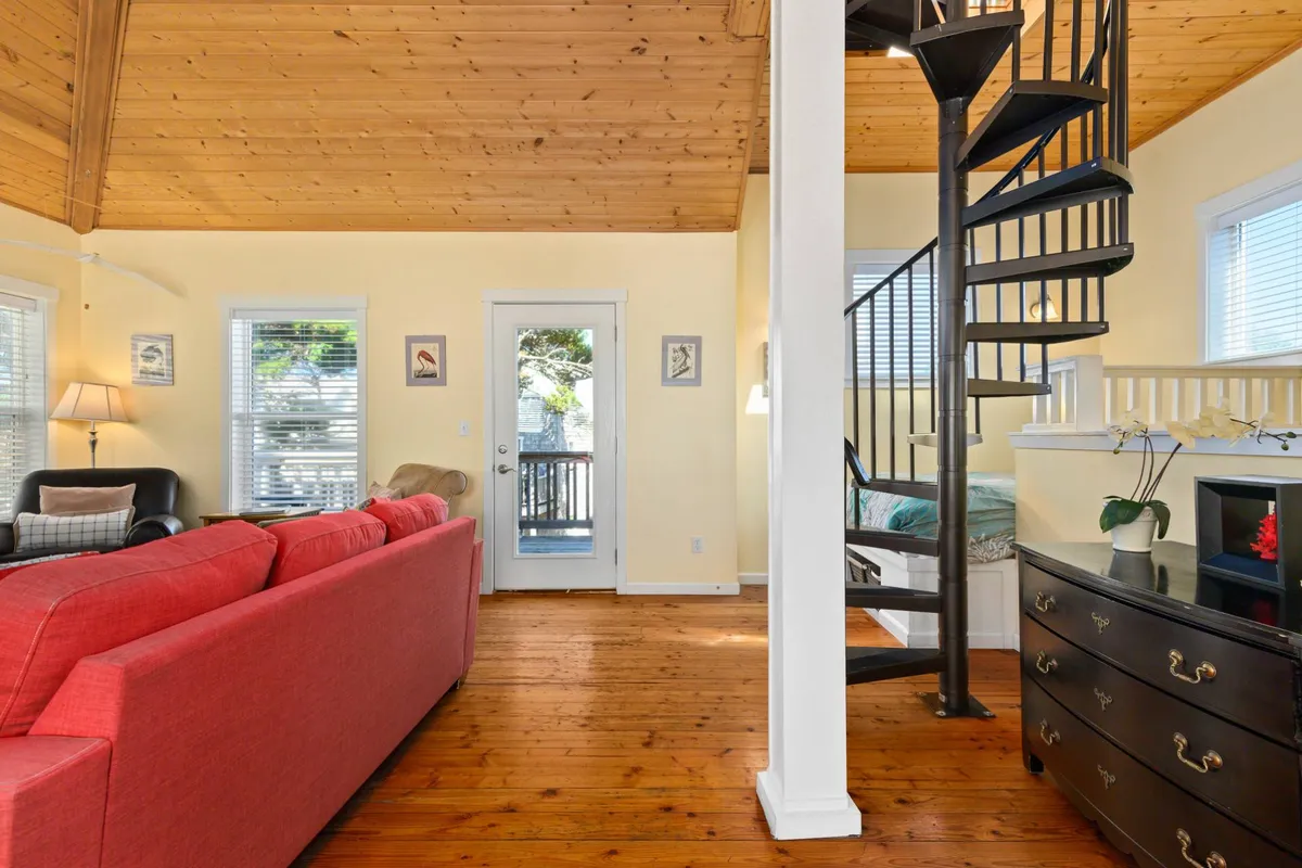 This interior shot features the spiral staircase, a red sofa, wooden flooring, and a door leading outside. The staircase is the focal point—immediately conveying the journey up to the crow’s nest, blending playfulness with architectural intrigue. The bright, welcoming living room area suggests spaces for relaxation and communal activities, supporting the narrative about family fun and gaming nights.