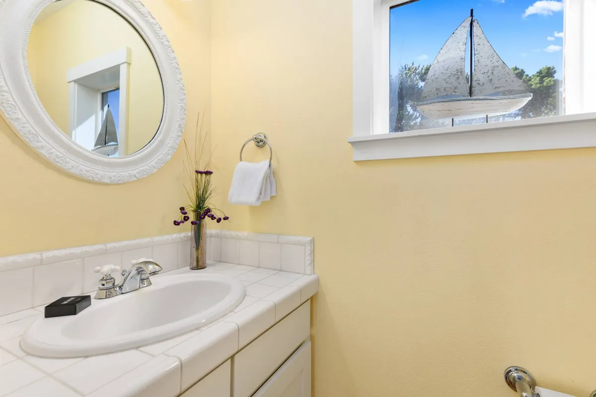 A fresh, calming bathroom scene with a round mirror, a stylish sink, a sailboat decoration, a towel rack, and a flower arrangement, radiating a peaceful and rejuvenating mood.